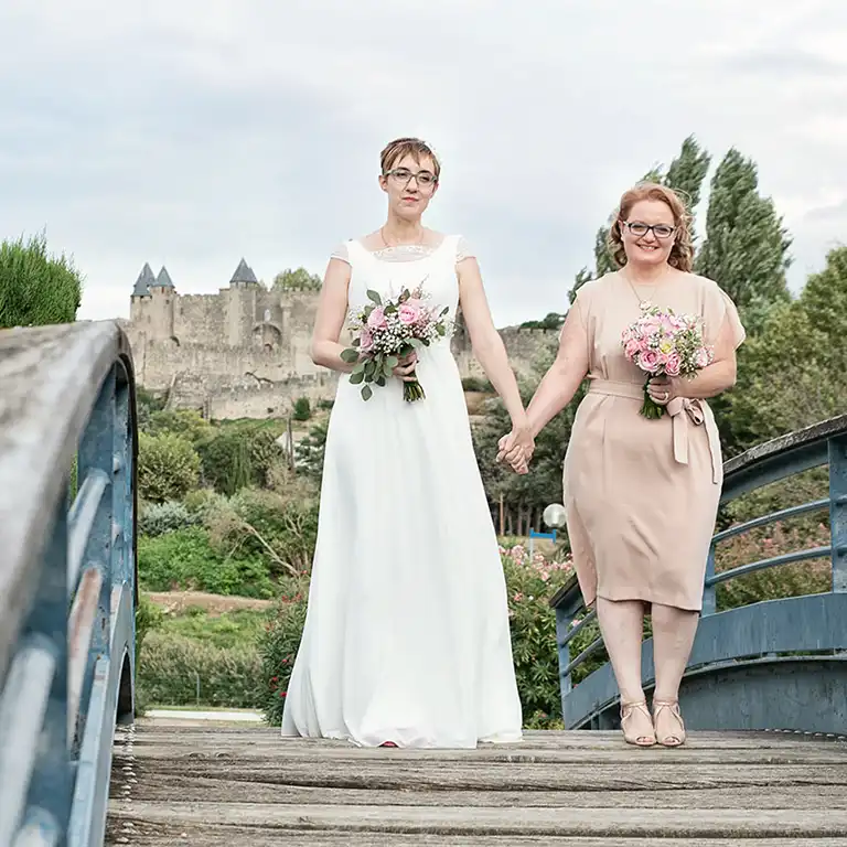Couple de femmes main dans la main devant les remparts de la Cité de Carcassonne, douceur d’un amour partagé